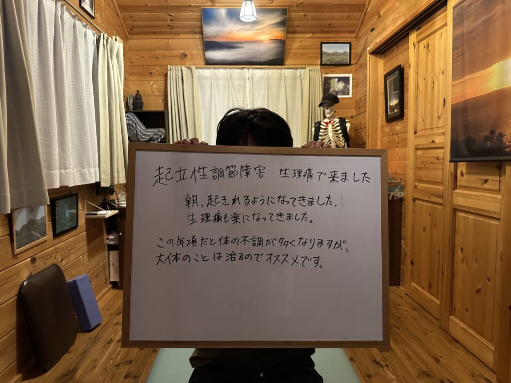 起立性調節障害と生理痛で来院している女子高生が施術後の変化を書いたホワイトボードを持っている様子